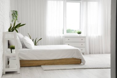 Rahat yatağı, rafları ve pencerenin yanındaki çekmeceleri olan modern yatak odası.