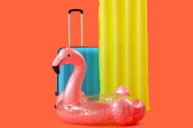 Şişme yüzük, yüzme şiltesi ve turuncu arka planda bavul. Seyahat kavramı