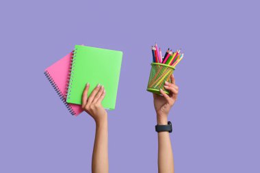 Mavi arkaplan üzerinde not defterleri ve kırtasiye malzemesi olan kadın elleri