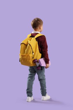 Sarı sırt çantalı, kaykaylı, leylak arka planda küçük bir okul çocuğu.