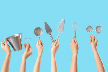 Mavi arka planda farklı pişirme aletleri olan kadın elleri