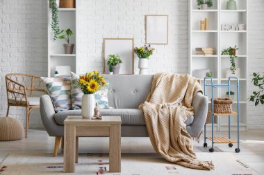 Yastıklı kanepe, ekose ve vazodaki yabani çiçekler oturma odasındaki sehpanın üzerinde.