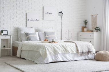 Yatak odasının içinde lamba, kahvaltı ve yatağın üstünde kitaplar var.