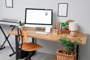 Gri duvar yakınında modern bilgisayar, sentezleyici ve ev bitkilerine sahip şık bir iş yeri