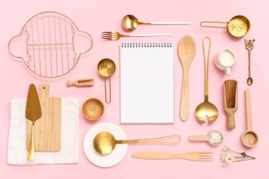 Boş tarif kitabı ve pembe arka planda farklı mutfak gereçleri olan kompozisyon