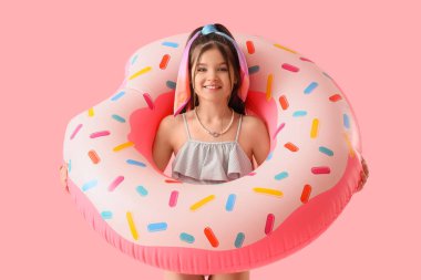 Pembe arka planda donut şekilli yüzme yüzüğü olan tatlı bir kız.