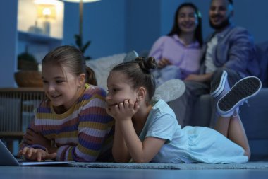 Bilgisayarlı şirin kız kardeşler ve akşam evde çizgi film izleyen aileler.