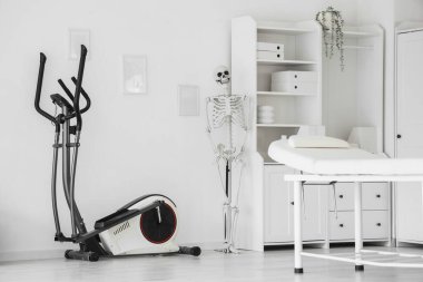 Koltuğu, egzersiz bisikleti ve insan iskeleti olan bir fizyoterapist ofisi.