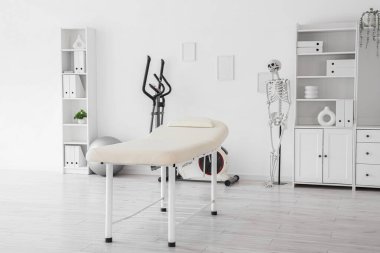 Koltuğu, egzersiz bisikleti ve insan iskeleti olan bir fizyoterapist ofisi.