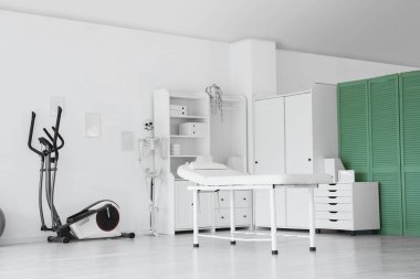 Koltuğu, egzersiz bisikleti ve insan iskeleti olan bir fizyoterapist ofisi.