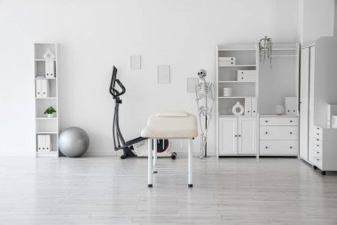 Koltuğu, egzersiz bisikleti ve insan iskeleti olan bir fizyoterapist ofisi.