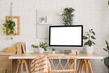 Ofiste beyaz tuğla duvarın yanında boş bilgisayar monitörü ve yeşil bitkileri olan işyeri