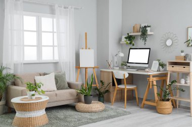 Interior of light office with workplace, sofa and green plants