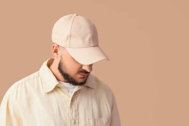 Bej arka planda şık şapkalı yakışıklı bir genç.