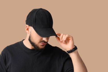 Bej arka planda şık şapkalı yakışıklı bir genç.