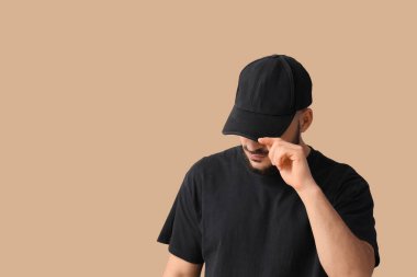 Bej arka planda şık şapkalı yakışıklı bir genç.