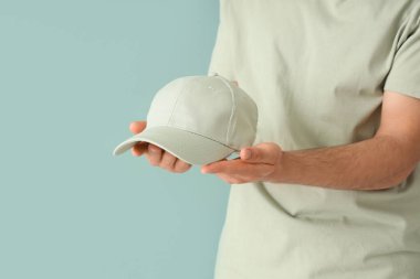 Genç adam yeşil arka planda şık bir şapka tutuyor.