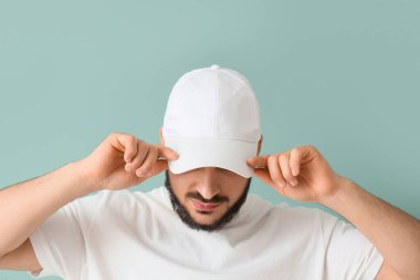 Mavi arka planda şık şapkalı yakışıklı bir genç.