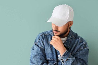 Mavi arka planda şık şapkalı yakışıklı bir genç.