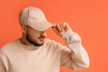 Turuncu arka planda şık şapkalı yakışıklı bir genç.