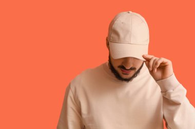 Turuncu arka planda şık şapkalı yakışıklı bir genç.