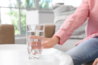 Oturma odasında bir bardak su içen sevimli küçük çocuk.