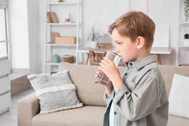 Oturma odasında su içen tatlı küçük çocuk.