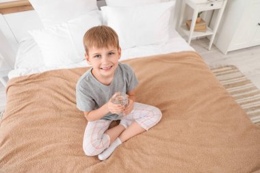 Yatak odasında bir bardak suyu olan şirin bir çocuk.