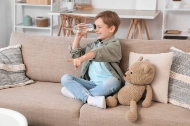 Oturma odasındaki bir şeyi işaret eden dürbün olarak su şişesi olan şirin çocuk.