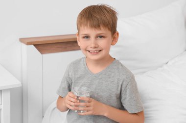 Yatak odasında bir bardak suyu olan şirin bir çocuk.