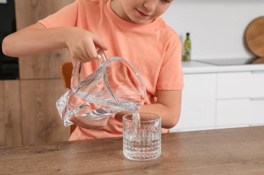 Tatlı küçük çocuk mutfaktaki sürahide bardaklara su dolduruyor.