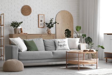 Gri kanepe, ahşap masa ve bitkilerle aydınlık oturma odasının içinde.