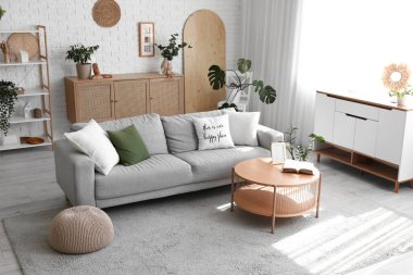 Gri kanepe, ahşap masa ve bitkilerle aydınlık oturma odasının içinde.