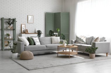 Gri kanepeler, masa ve yeşil bitkilerle aydınlık oturma odasının içinde.