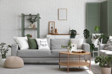 Gri kanepeler, masa ve yeşil bitkilerle aydınlık oturma odasının içinde.