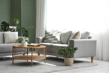 Gri kanepeler, masa ve yeşil bitkilerle aydınlık oturma odasının içinde.