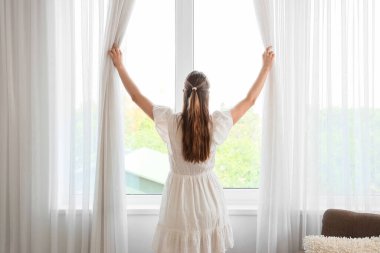 Odada ışık perdeleri açan genç bir kadın.