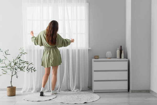 Молодая женщина возле светлого занавеса в комнате, вид сзади