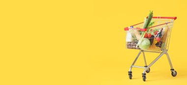 Sarı zemin üzerinde farklı taze ürünlerle dolu alışveriş arabası metin için yer var.