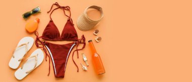 Şık bir mayo, bir şişe kokteyl ve turuncu arka planda plaj aksesuarları.