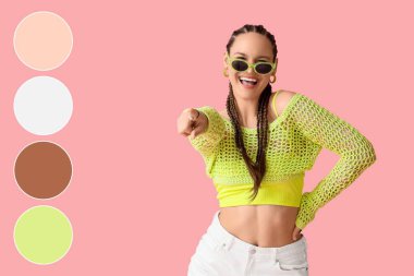 Afrika örgülü ve güneş gözlüklü zarif genç bir kadın pembe arka plandaki izleyiciyi işaret ediyor. Farklı renk desenleri