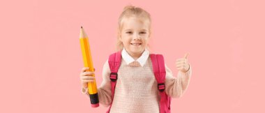 Büyük kalemle pembe arka planda baş parmağını gösteren sevimli küçük okul kızı.