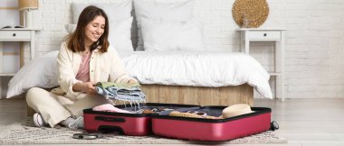 Güzel genç bir kadın, açık otel odasında bavulunu giysileriyle açıyor.