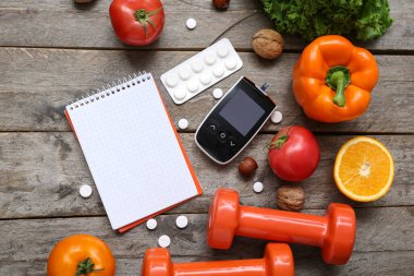 Boş defter, glukometre, haplar ve ahşap zemin üzerinde sağlıklı ürünler içeren kompozisyon