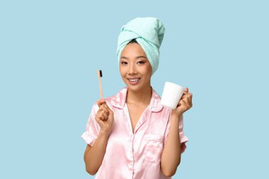 Mavi arka planda diş fırçası ve fincanı olan genç Asyalı kadın.