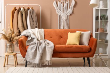 Modern oturma odasının içinde kahverengi kanepe, sıcak battaniye ve askıda asılı giysiler.