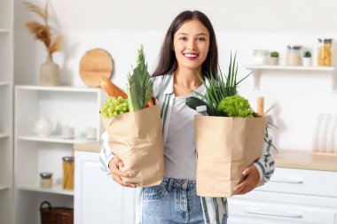 Mutfakta içi taze yiyecek dolu alışveriş torbalarıyla genç Asyalı kadın.