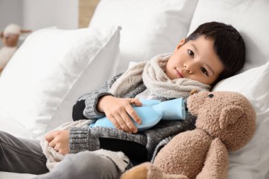 Yatak odasında sıcak su şişesiyle yatan küçük Asyalı çocuk.