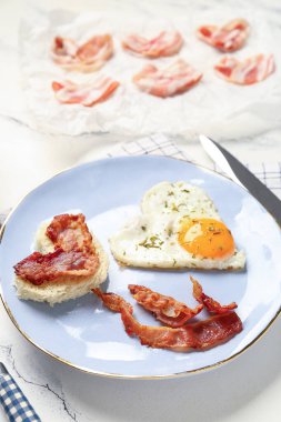 Plate with tasty bacon, hearts made of fried egg and bread on light background, closeup
