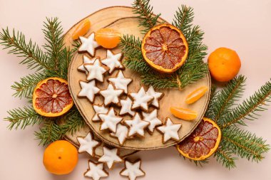 Mandarin, kurutulmuş portakal ve köknar dallarıyla bej arka planda yıldız şeklinde zencefilli kurabiye tahtası.